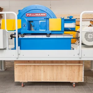 Langholzzerspaner der Marke Pallmann: große blaue Schneidscheibe aufgeständert über einer Holzkiste zur Produktion von Holzspänen in einer Prüfumgebung.