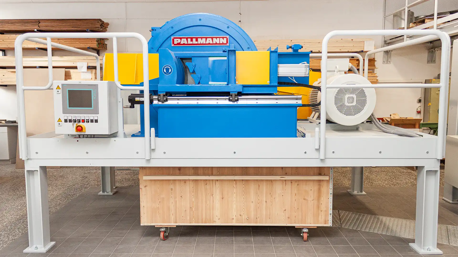 Langholzzerspaner der Marke Pallmann: große blaue Schneidscheibe aufgeständert über einer Holzkiste zur Produktion von Holzspänen in einer Prüfumgebung.