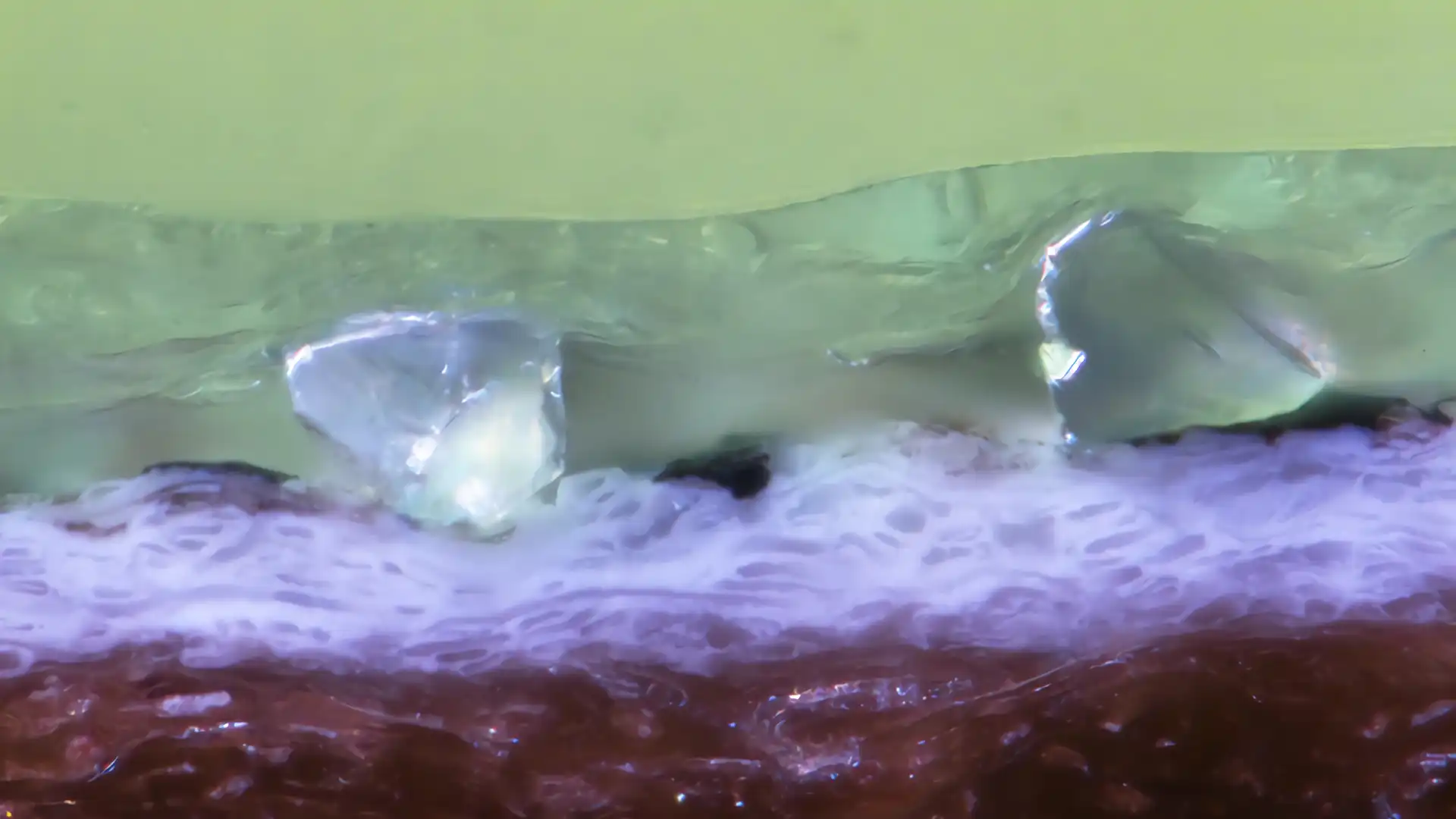 Mikroskopische Querschliffaufnahme (100 µm Maßstab) einer Schicht mit eingebetteten Korundpartikeln zur Vermessung von Schichtdicken und Untersuchung mikroskopischer Strukturen.