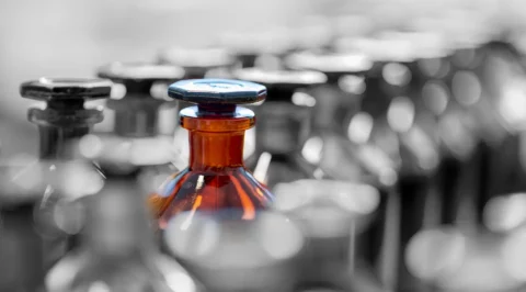 This photograph shows a row of laboratory bottles, with a brown bottle with a cap in focus. It symbolises the use of chemicals and reagents in scientific experiments.