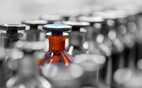 Diese Aufnahme zeigt eine Reihe von Laborflaschen, wobei eine braune Flasche mit Verschluss im Fokus steht. Sie symbolisiert den Einsatz von Chemikalien und Reagenzien in wissenschaftlichen Experimenten.