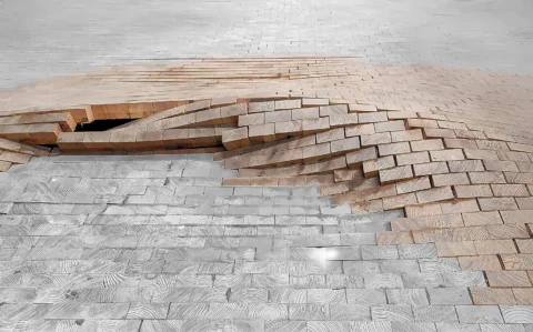 Schadensanalyse an einem Holzfußboden: Stirnholz-/Klötzchenparkett ist großflächig aufgewölbt; einzelne Holzklötze stehen hoch und bilden eine kraterartige Vertiefung.