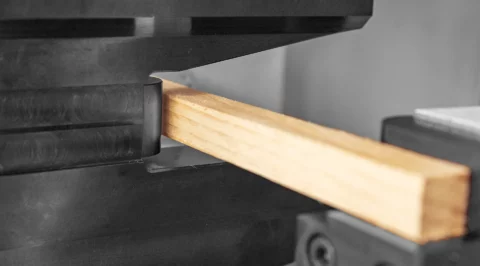 Close-up of a square wooden rod clamped in black metal jaws – part of a physical test setup for investigating mechanical properties.