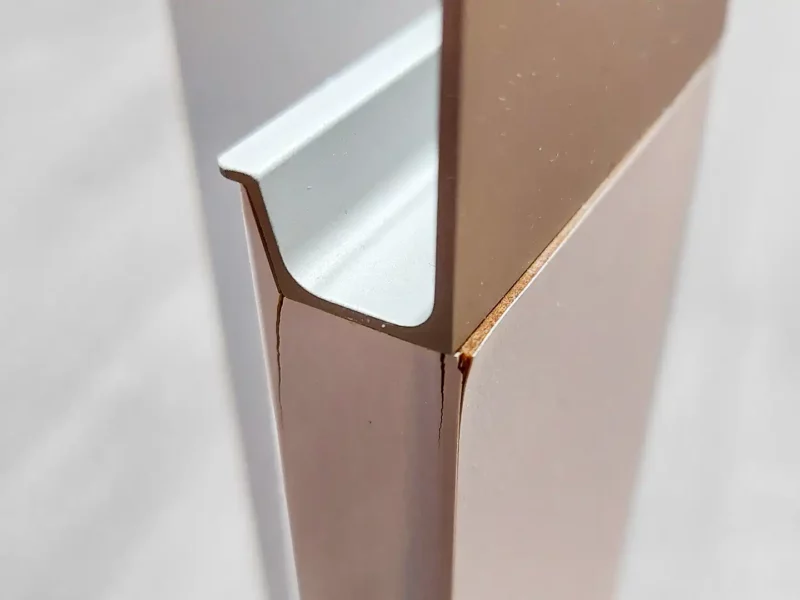 Makroaufnahme einer Möbelkante: neben einem eingesteckten Metall-/Aluprofil zeigen sich Spannungsrisse in der dekorativen Schicht/Edgebanding .