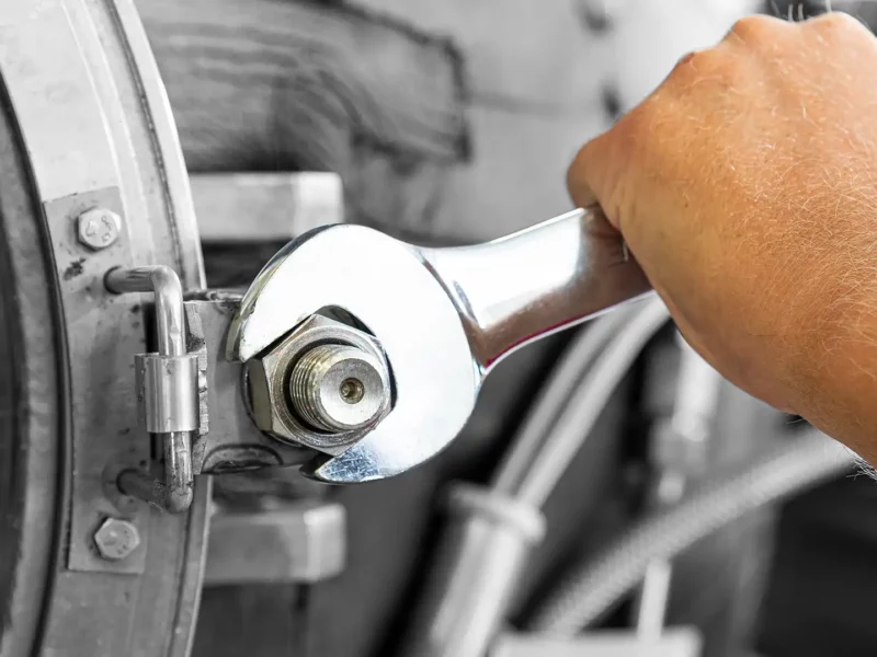 Hand zieht mit einem Schraubenschlüssel eine Verschraubung an einer Metallanlage fest.