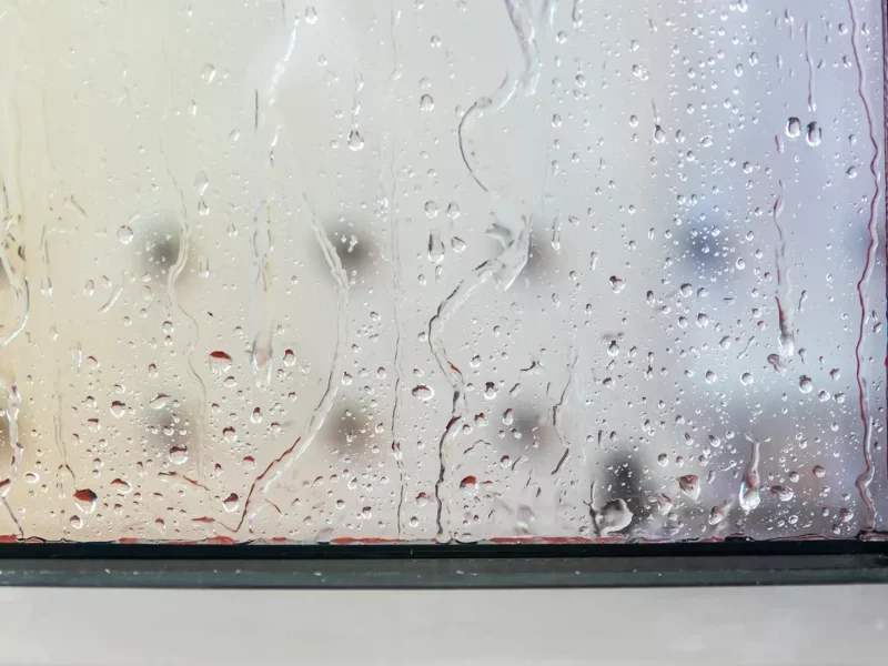 Nahaufnahme einer Fensterscheibe mit Regentropfen und Rinnspuren an der unteren Kante.