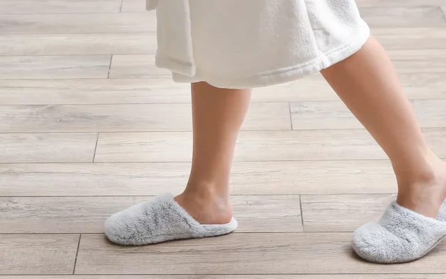 Person mit Hausschuhen auf hellem Holzfußboden im Innenraum