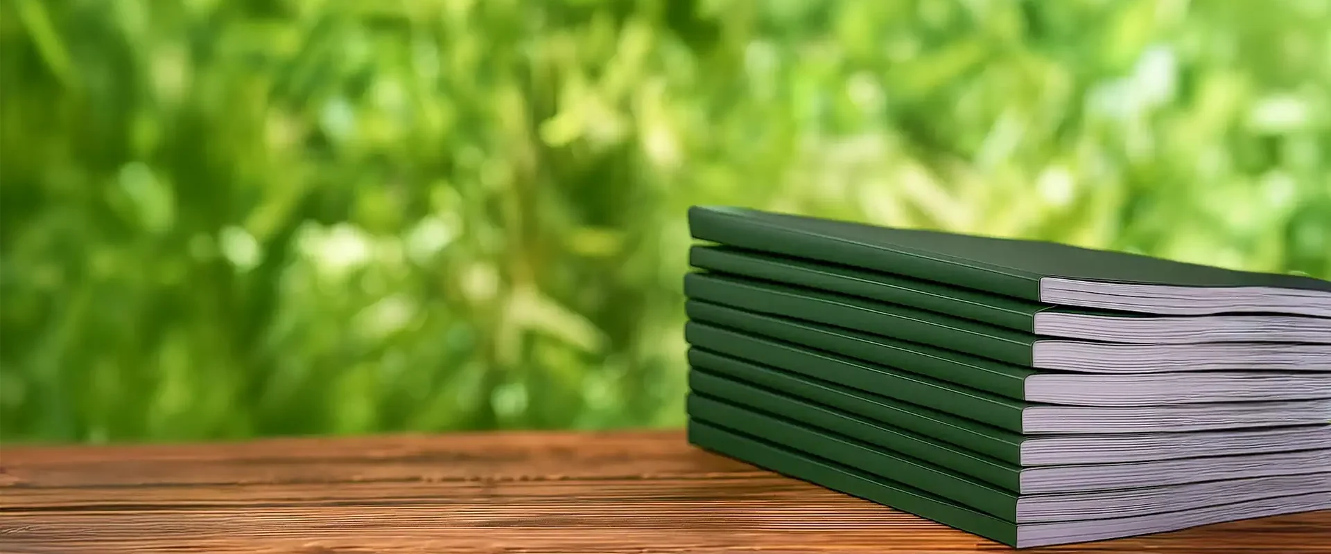 Gestapelte dunkelgrüne Broschüren auf einer Holzoberfläche vor unscharf grünem Naturhintergrund – Symbol für nachhaltige Publikationen.