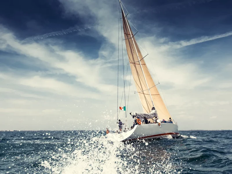 Symbolbild zur Forschungskoordination: Segelyacht mit Crew auf offener See, Gischt im Vordergrund und Segel im Wind vor weitem Himmel.