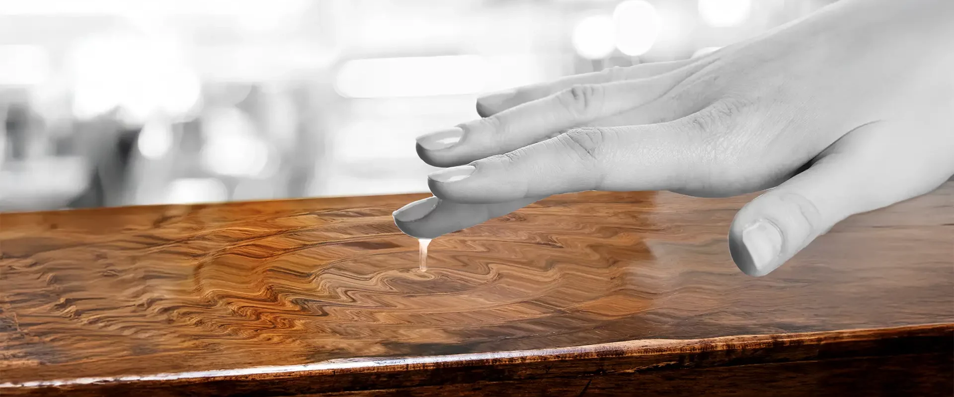 Ein Finger berührt den Transparentlack einer reich gemaserten Holzoberfläche und löst dadurch kleine Wellen aus.