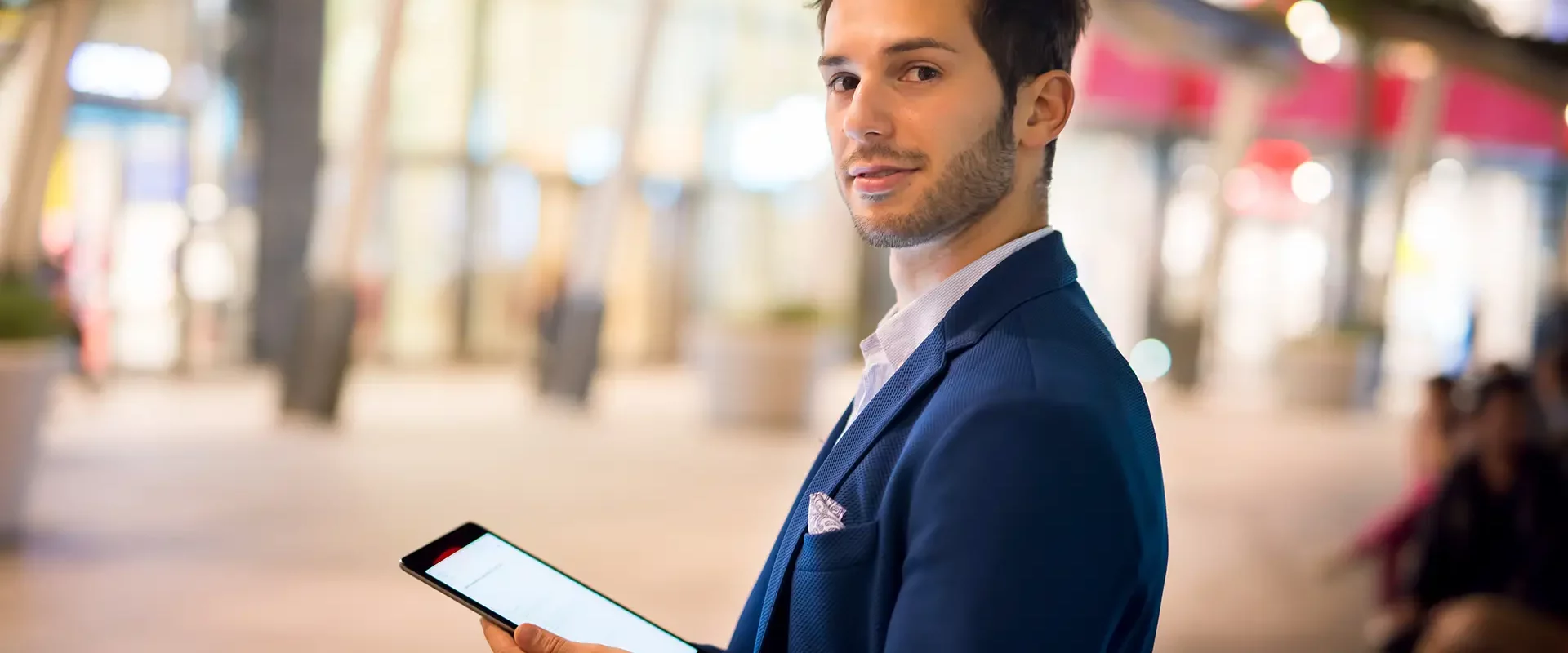 Mann im Anzug hält Tablet in moderner Shopping-Passage