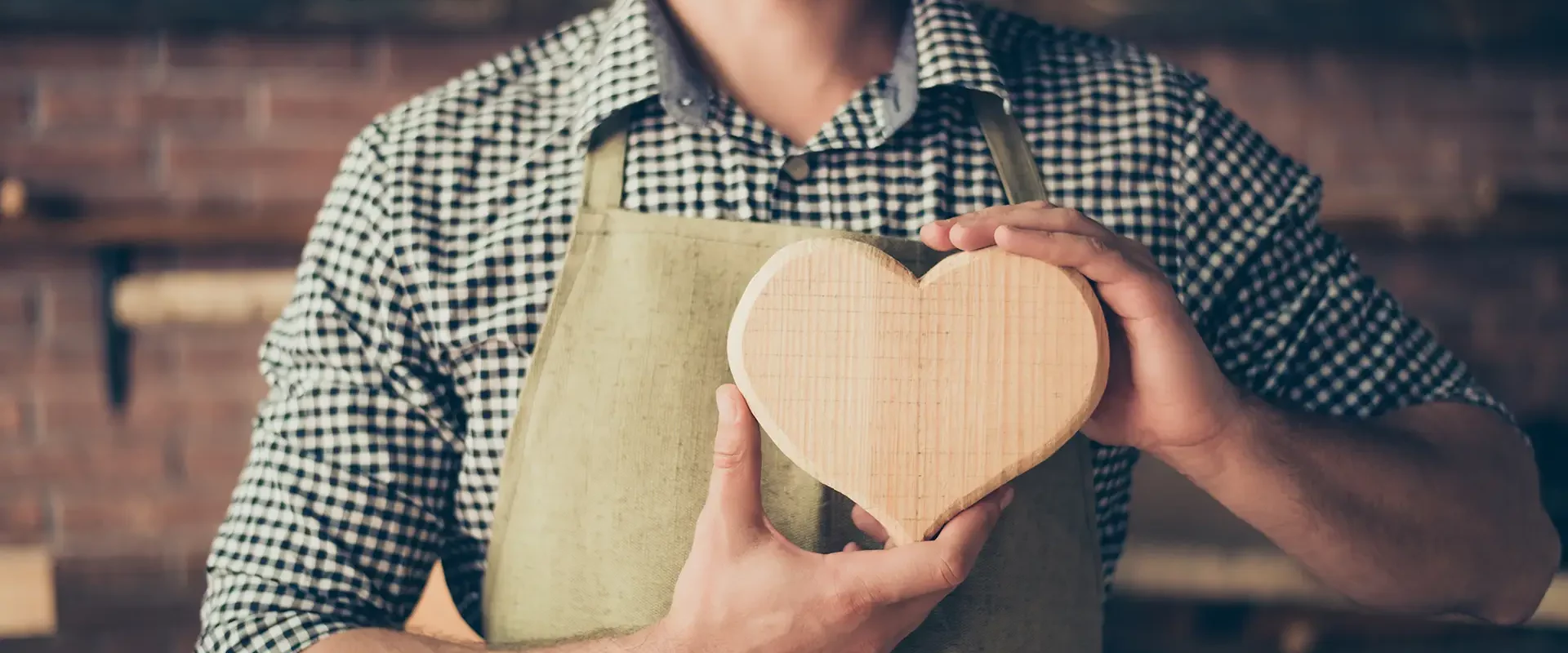 Handwerker hält herzförmiges Holzstück in der Werkstatt