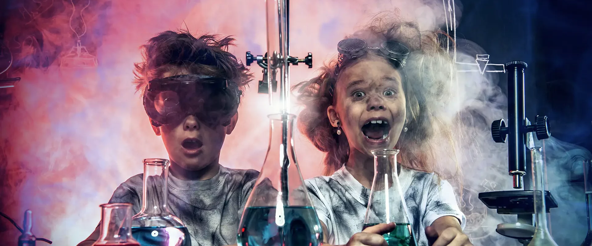 Zwei Kinder mit Schutzbrillen machen ein Chemie-Experiment mit Laborgläsern und Rauch