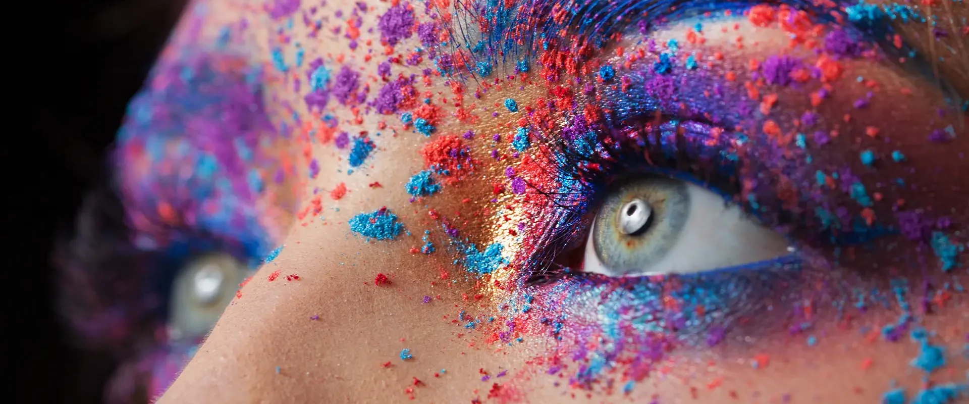 Nahaufnahme eines Auges mit buntem Farbpigment-Make-up in Blau, Pink und Gold
