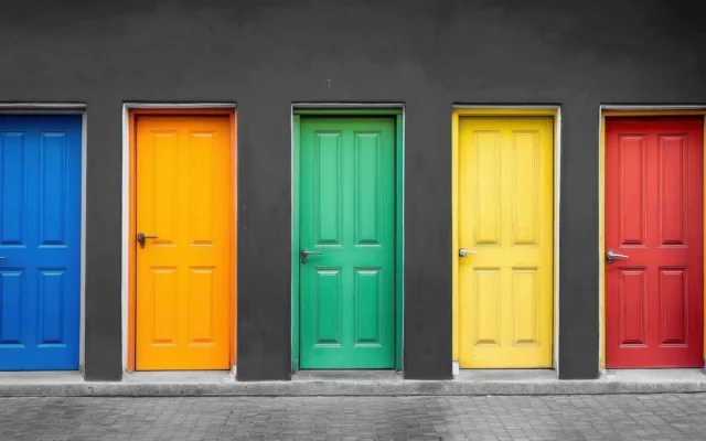 Fünf farbige Holztüren in Blau, Orange, Grün, Gelb und Rot in dunkler Wand