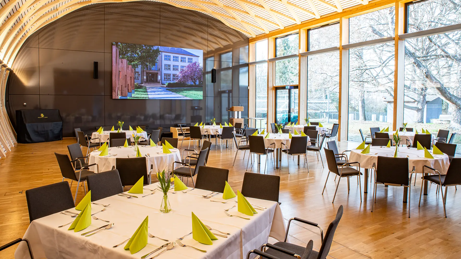 Veranstaltungssaal IHD mit moderner Holzarchitektur, gedeckten runden Tischen und großer Fensterfront