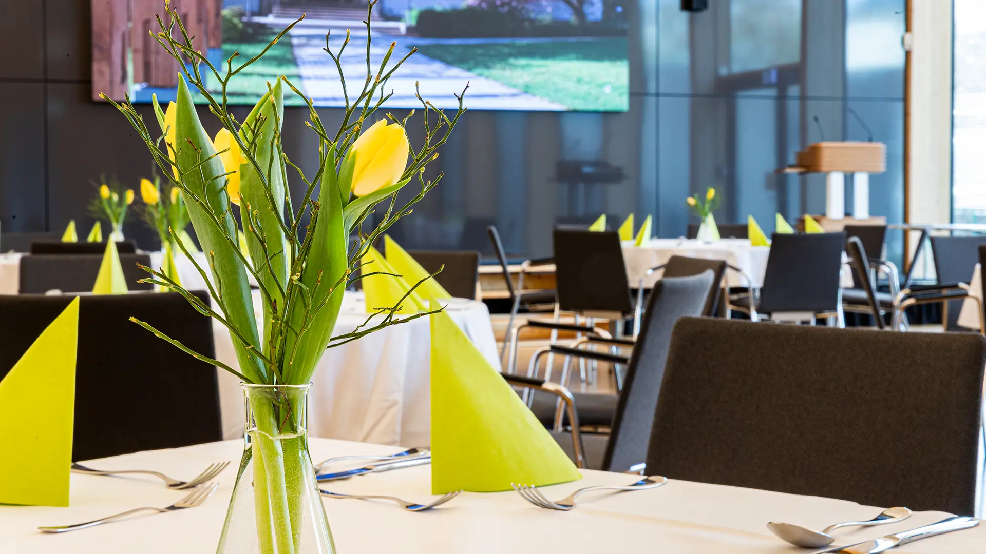 Gedeckter Veranstaltungstisch mit Tulpenvase und gefalteten Servietten im modernen Holzsaal