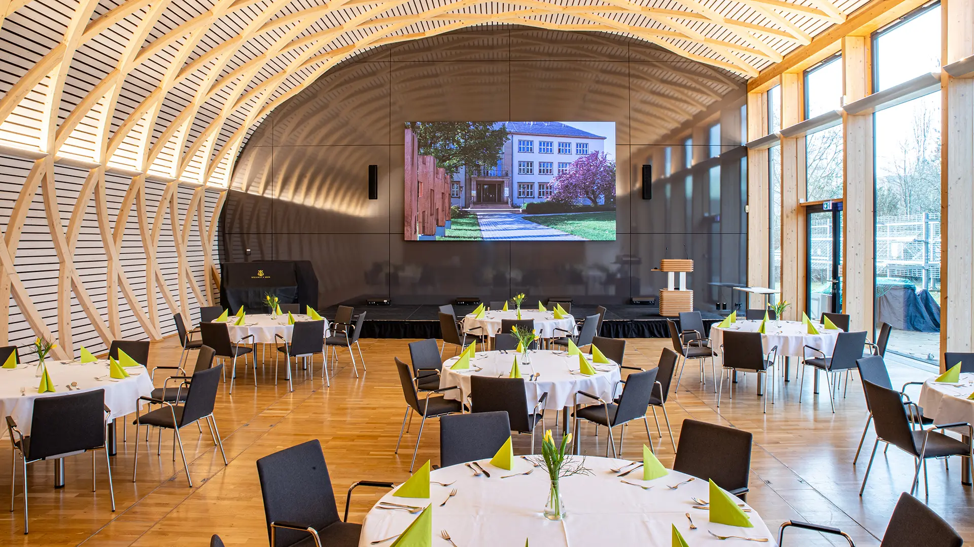 Veranstaltungssaal IHD mit moderner Holzarchitektur, gedeckten runden Tischen und großer Fensterfront