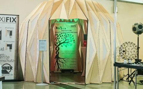 Messestand des Instituts für Holztechnologie Dresden mit kuppelförmiger Holzstruktur und beleuchtetem IHD-Banner auf einer Fachmesse