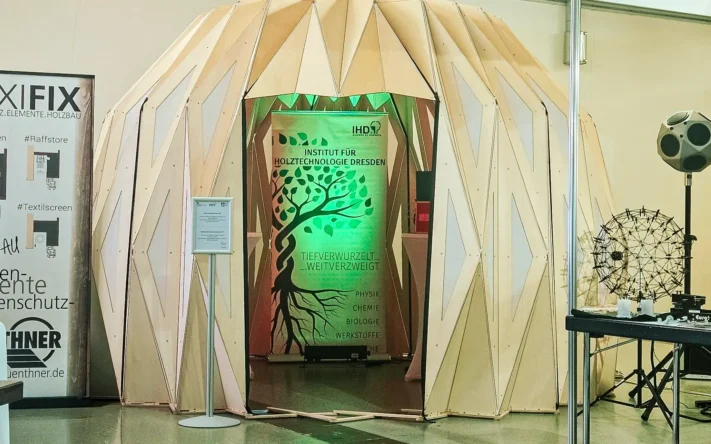 Messestand des Instituts für Holztechnologie Dresden mit kuppelförmiger Holzstruktur und beleuchtetem IHD-Banner auf einer Fachmesse