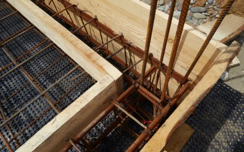 Detailaufnahme einer Baustelle mit Holzschalung und Stahlbewehrung zur Vorbereitung eines Stahlbetonbauteils. Die Konstruktion zeigt die Anordnung der Bewehrungsstäbe innerhalb der Schalung.